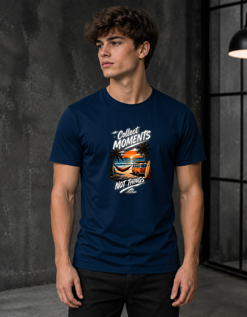 A man wearing a Navy Blue short-sleeve graphic t-shirt with the text 'Collect Moments Not Things' and a colorful beach sunset print, standing in a dark gray studio setting.