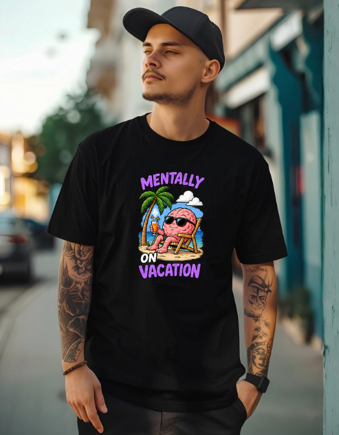 A man wearing a black graphic t-shirt with a colorful cartoon design of a pink brain on a beach chair and the text 'MENTALLY ON VACATION'. He is also wearing a black baseball cap and has visible tattoos on both arms, standing outdoors against a blurred street background.