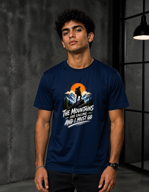 A man wearing a Navy Blue short-sleeve graphic t-shirt with a mountain and sunset design and the text 'THE MOUNTAINS ARE GORGING AND I MUST GO'.