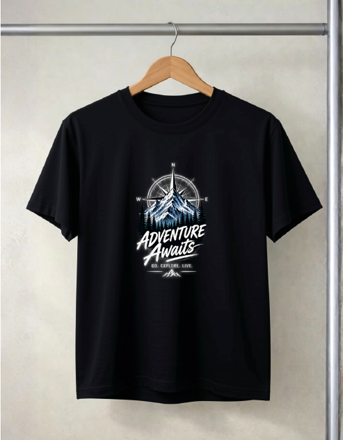 A black short-sleeve t-shirt hanging on a wooden hanger against a light beige wall. The shirt features a graphic print on the chest with a compass, mountain illustration, and the text 'ADVENTURE AWAITS' in white and blue.