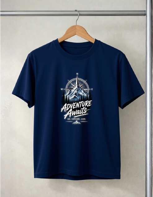 A navy blue short-sleeve t-shirt hanging on a wooden hanger against a light beige textured wall. The shirt features a graphic print on the chest with a compass, mountain, and the words 'Adventure Awaits' in white and light blue.