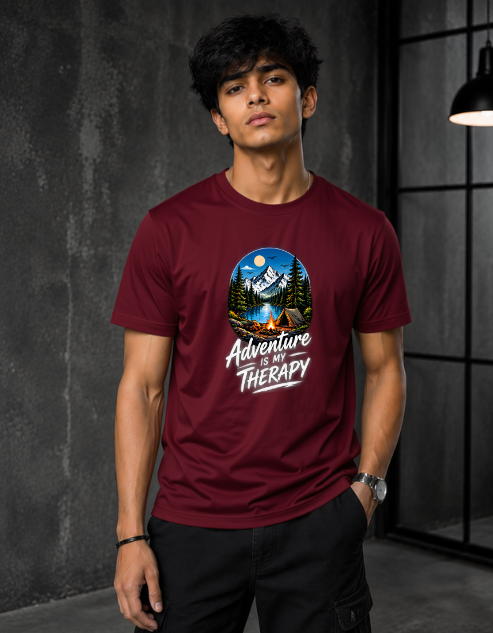 A man wearing a maroon crewneck t-shirt with a circular graphic of a mountain campsite and the text 'Adventure is Therapy'.