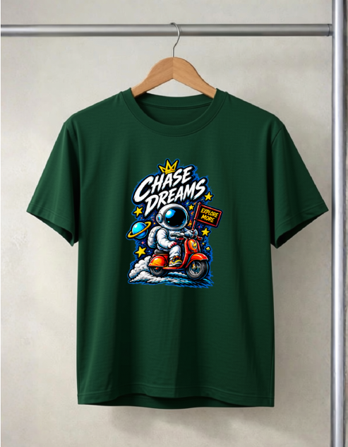 A Bottle green short-sleeve t-shirt hanging on a wooden hanger against a light gray wall. The shirt features a colorful graphic print of an astronaut riding a red motorcycle with the text 'Chase Dreams' and a small sign that reads 'Ride with Me'.