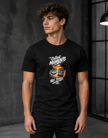 A man wearing a black short-sleeve graphic t-shirt with the text 'Collect Moments Not Things' and a colorful beach sunset print, standing in a dark gray studio setting.