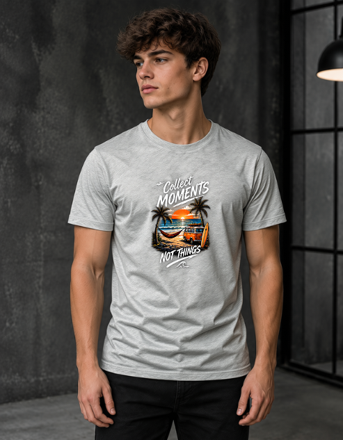 A man wearing a light grey Melange heather t-shirt with a graphic print that reads 'Collect MOMENTS NOT THINGS' around a beach sunset illustration, standing in a dark gray studio setting.