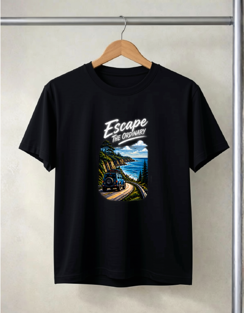A Black color short-sleeve t-shirt hanging on a wooden hanger against a light gray wall. The shirt features a graphic print on the front with the text 'Escape The Ordinary' above an illustration of a train traveling along a scenic coastal mountain road.