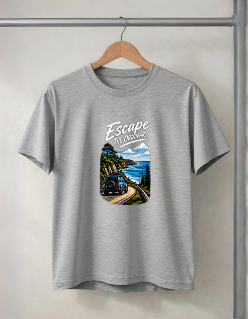 A grey Melange heather crewneck t-shirt hanging on a wooden hanger from a metal clothing rack. The shirt features a graphic print on the front with the text 'Escape THE ORDINARY' above an illustration of a vintage train traveling along a coastal mountain road with blue skies and ocean.