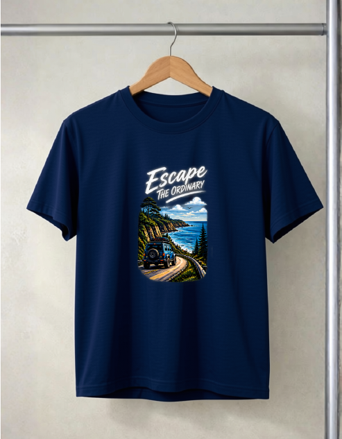 A navy blue short-sleeve t-shirt hanging on a wooden hanger against a textured beige wall. The shirt features a graphic print on the front with the text 'Escape The Ordinary' above an illustration of a train traveling along a scenic coastal mountain road.