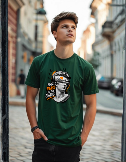 A man wearing a bottle green graphic t-shirt with a portrait of Galen Erskine and the text 'FIND PEACE IN CHAOS' standing in a cobblestone street.
