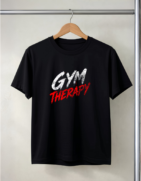 A black short-sleeve t-shirt hanging on a wooden hanger against a light gray wall. The shirt features a distressed graphic on the chest that reads 'GYM THERAPY' in white and red lettering.