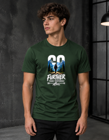 A man wearing a bottle green graphic t-shirt with a mountain and forest design and the text 'GO FURTHER THAN YESTERDAY'.