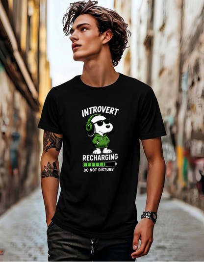 A man wearing a black graphic t-shirt with a cartoon dog wearing green headphones and the text 'INTROVERT RECHARGING DO NOT DISTURB', standing in a narrow city alleyway.