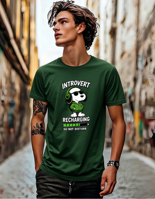 A man wearing a dark green graphic t-shirt with a cartoon dog wearing headphones and the text 'INTROVERT RECHARGING DO NOT DISTURB' in a narrow outdoor alleyway.