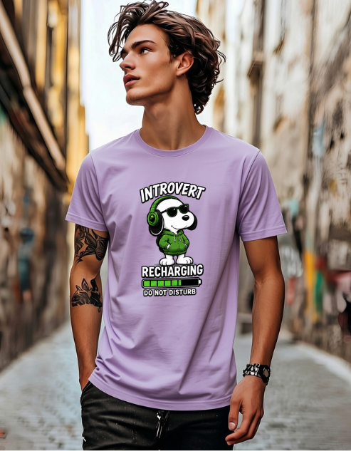 A man wearing a lavender graphic t-shirt with a cartoon dog wearing green headphones and the text 'INTROVERT RECHARGING DO NOT DISTURB'. The man is standing in a narrow, blurred urban alleyway.
