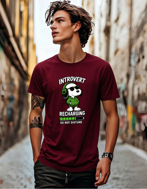 A man wearing a maroon graphic t-shirt with a cartoon panda wearing green headphones and the text 'INTROVERT RECHARGING DO NOT DISTURB', standing in a narrow street.