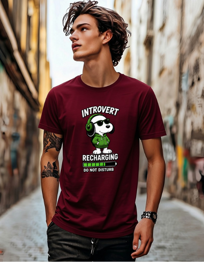 A man wearing a maroon graphic t-shirt with a cartoon panda wearing green headphones and the text 'INTROVERT RECHARGING DO NOT DISTURB', standing in a narrow street.