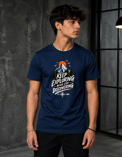 A man wearing a navy blue graphic t-shirt with a mountain and sun design and the text 'KEEP EXPLORING WHEN YOU'RE DISCOVERING'.