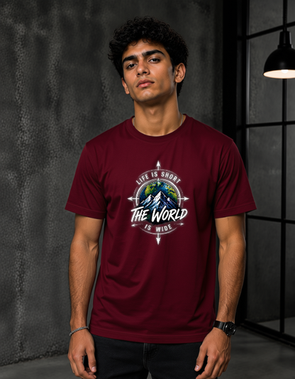 A man wearing a maroon short-sleeve t-shirt with a circular graphic on the chest that reads 'LIFE IS SHORT THE WORLD IS MIND' around a mountain and globe design, set against a dark gray textured wall.