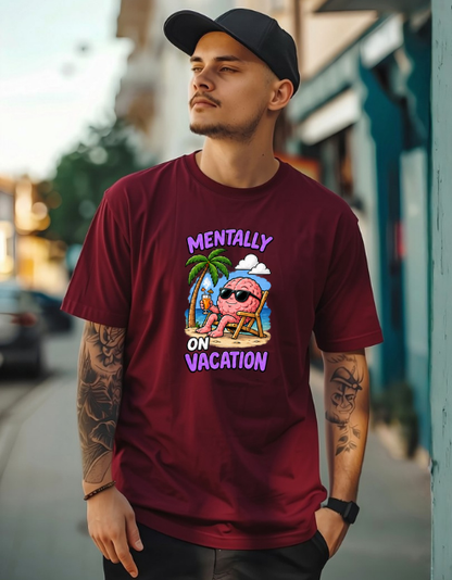A man wearing a maroon crewneck t-shirt with a colorful graphic of a pink brain on a beach chair and the text 'MENTALLY ON VACATION'. He is also wearing a black baseball cap and standing on a blurred street background.