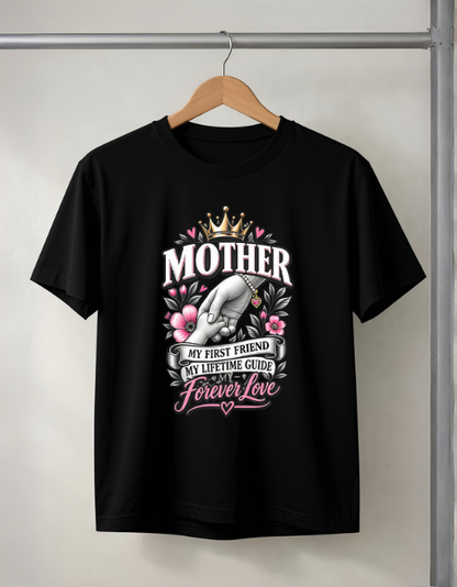 A black short-sleeve t-shirt hanging on a wooden hanger against a light gray wall. The shirt features a large graphic print on the front with the word 'MOTHER' in white, a gray cat wearing a crown, pink flowers, and text reading 'MY FIRST FRIEND MY LIFETIME GUIDE Forever Love'.