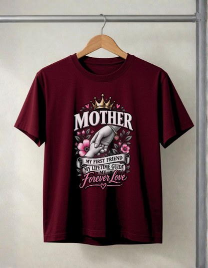 A maroon short-sleeve t-shirt hanging on a wooden hanger against a light gray wall. The shirt features a graphic print on the front with a hand holding a heart, a gold crown, pink flowers, and the text 'MOTHER MY FIRST FRIEND MY LIFETIME GUIDE AND MY Forever Love'.
