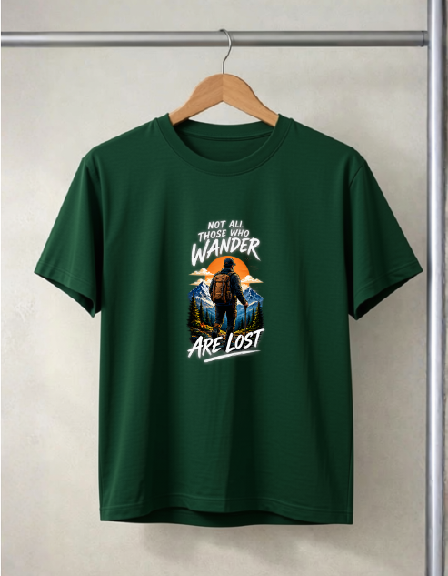 A Bottle green short-sleeve t-shirt hanging on a wooden hanger against a textured light gray wall. The shirt features a graphic print of a Bigfoot in a mountain landscape with the text 'NOT ALL THOSE WHO WANDER ARE LOST'.