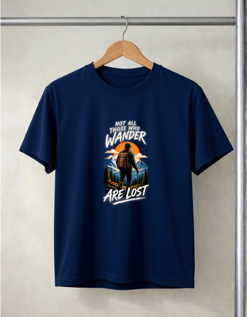 A navy blue short-sleeve t-shirt hanging on a wooden hanger against a light beige textured wall. The shirt features a graphic print on the front with a silhouette of a person hiking against a sunset, framed by mountains, with the text 'NOT ALL THOSE WHO WANDER ARE LOST'.