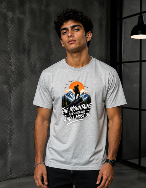 A man wearing a Grey Melange short-sleeve graphic t-shirt with a mountain and sunset design and the text 'THE MOUNTAINS ARE GORGING AND I MUST GO'.