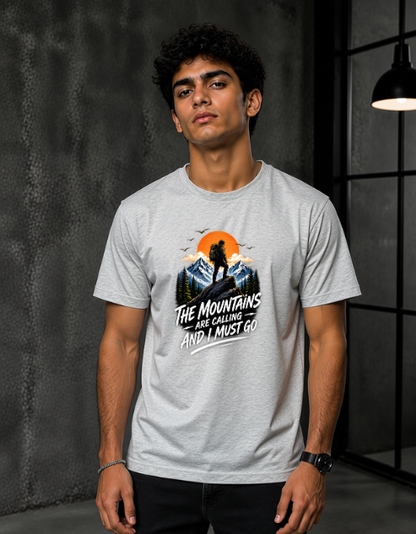 A man wearing a Grey Melange short-sleeve graphic t-shirt with a mountain and sunset design and the text 'THE MOUNTAINS ARE GORGING AND I MUST GO'.