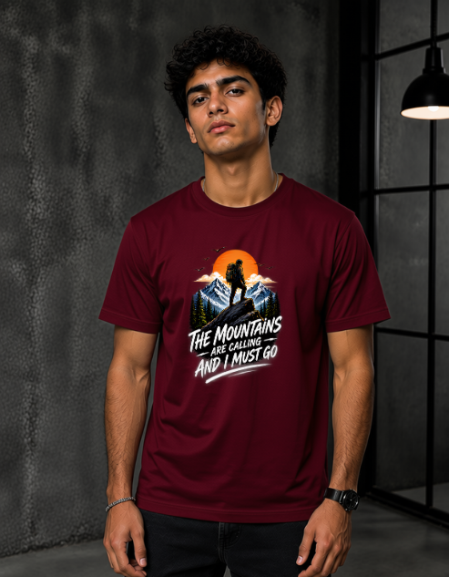 A man wearing a Maroon short-sleeve graphic t-shirt with a mountain and sunset design and the text 'THE MOUNTAINS ARE GORGING AND I MUST GO'.