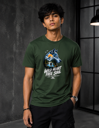 A man wearing a dark green crewneck t-shirt with a graphic of a blue wolf and the text 'WILD HEART FREE SOUL' on the front, set against a dark gray textured wall background.